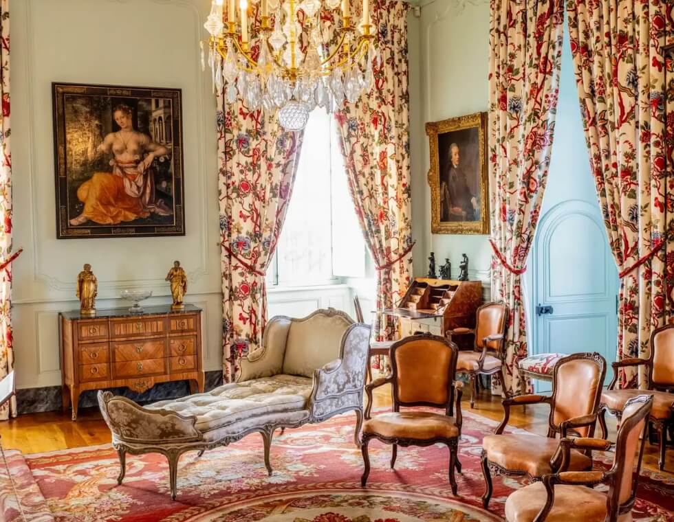 Interior of historic Hautefort Castle in Dordogne, France, with antique furniture, elegant drapes, and framed paintings.