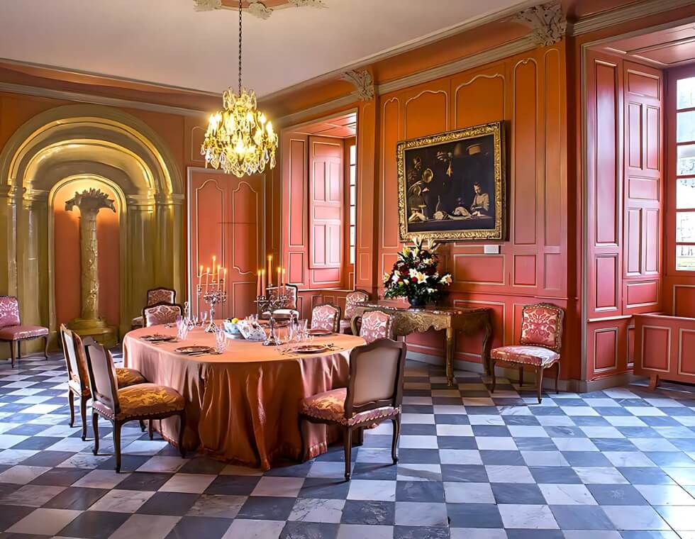 Villandry Castle dining room in France with a crystal chandelier, warm orange accents, and elegant antique upholstered chairs.