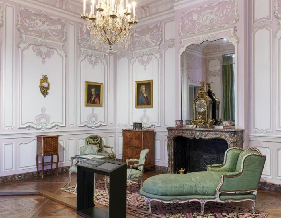 Staged historic home interior at the Carnavalet Museum in Paris, featuring ornate wood furniture and a crystal chandelier.