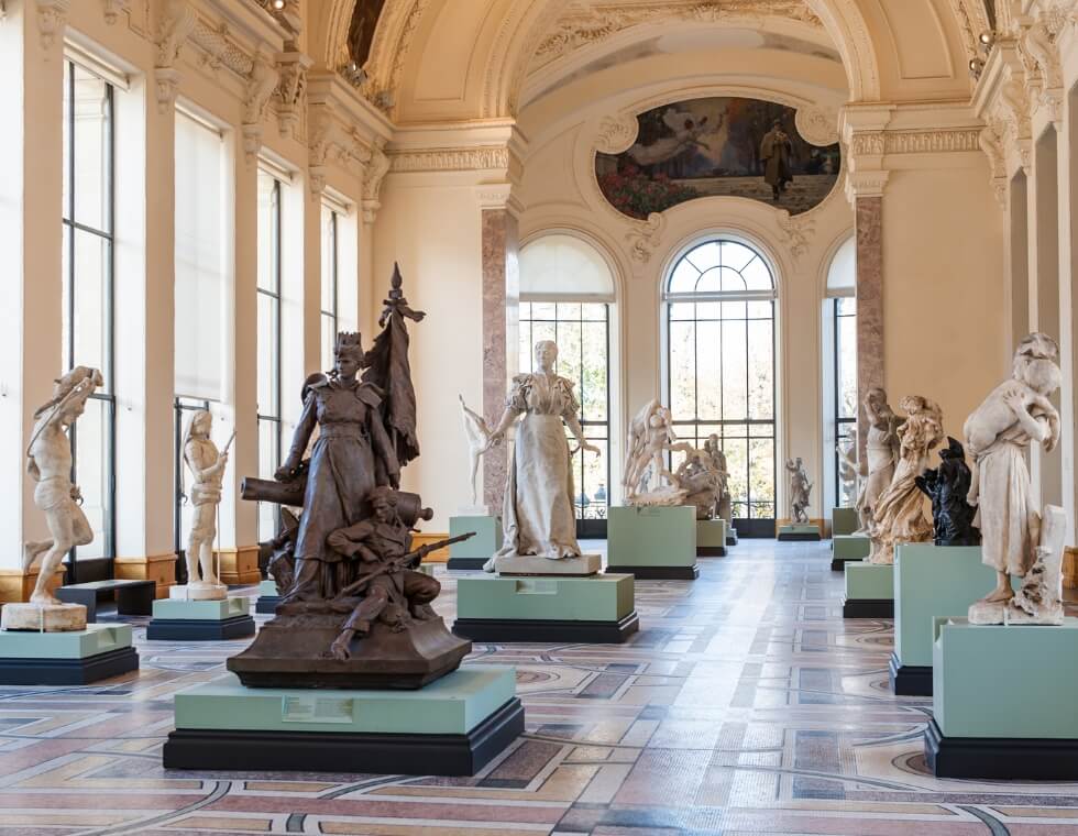 Petit Palais Museum in Paris, France, featuring marble and metal cast statues beneath historic painted ceilings.