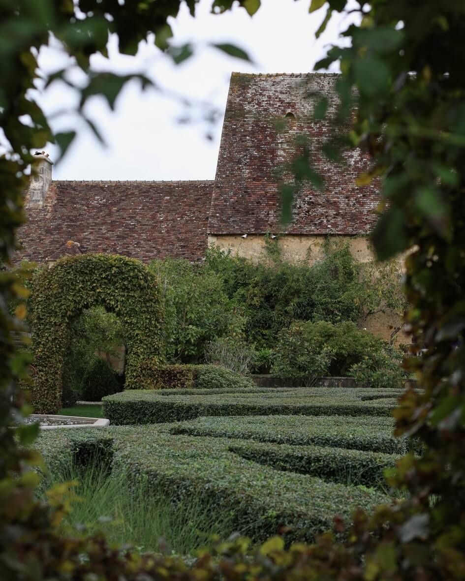 View of a traditional French garden with manicured hedges and lush green landscaping in Normandy.