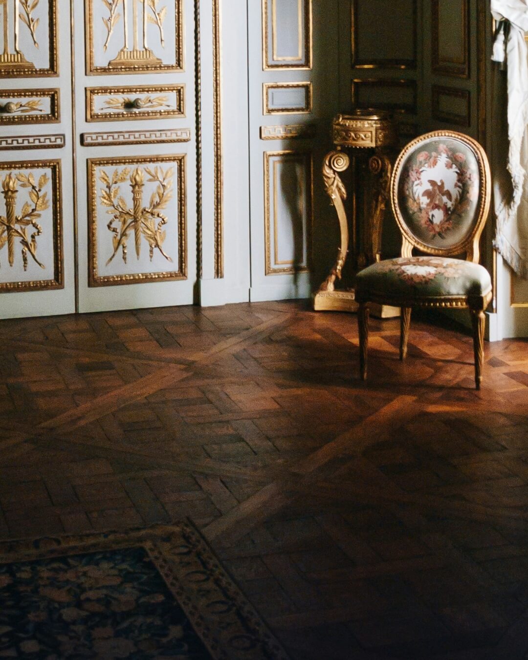 Parquet floors and an antique chair in a historic Parisian salon adorned with gold leaf.
