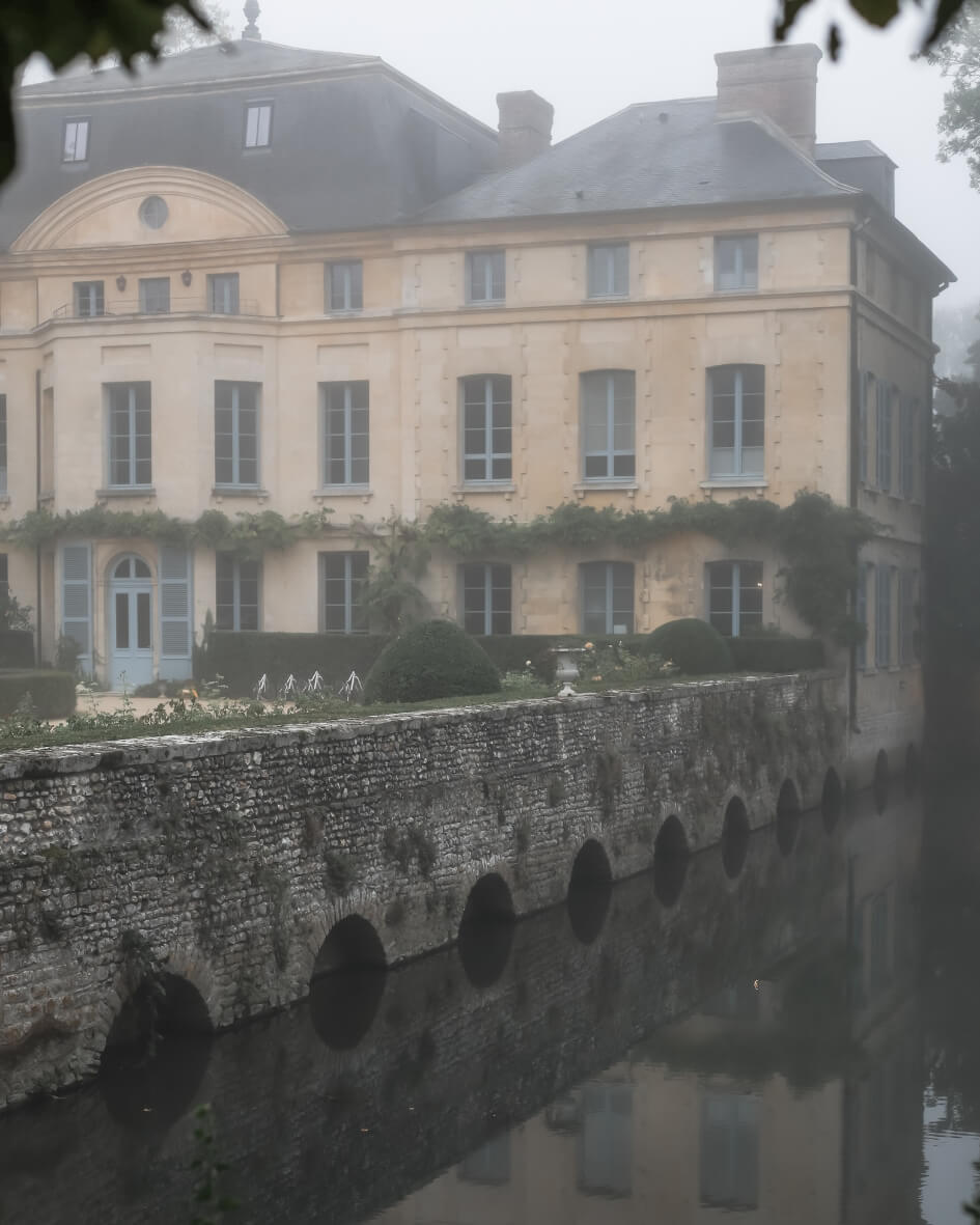 Entrance to the historic Domaine de Primard in Normandy, France, beside a still river.
