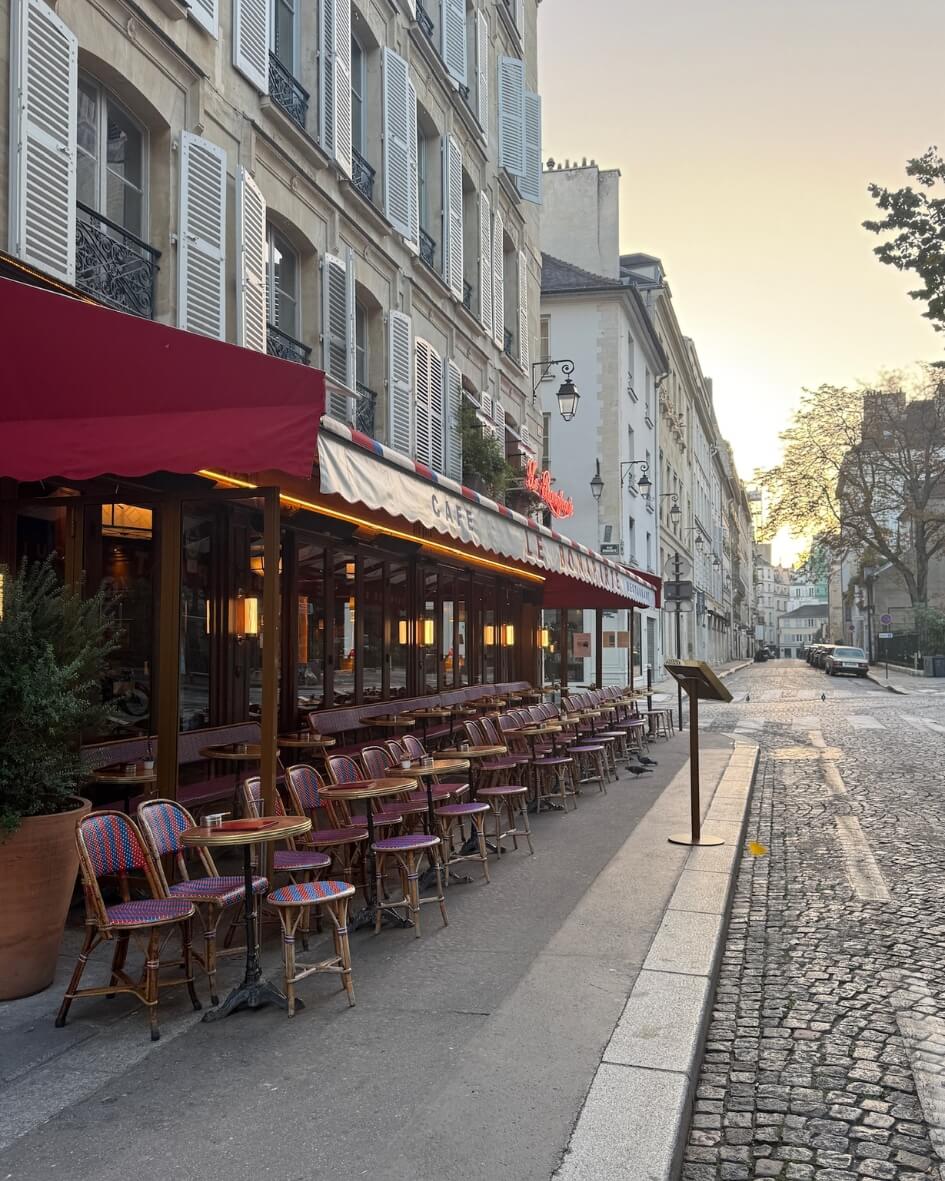 Parisian cafe and terrance lined with red bistro chairs beneath a red awning in autumn.