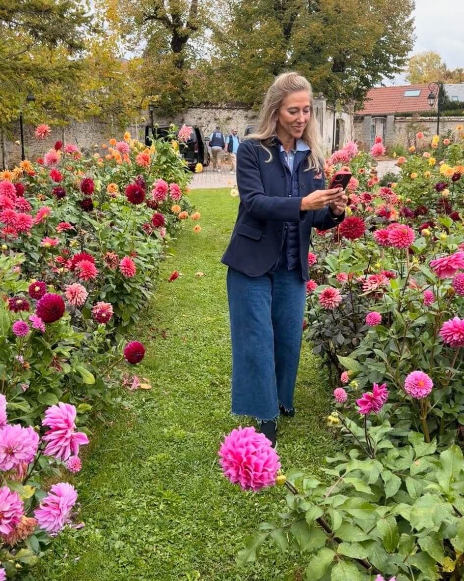 Stacey Caron standing beside blooming dahlias in a lush Normandy garden.