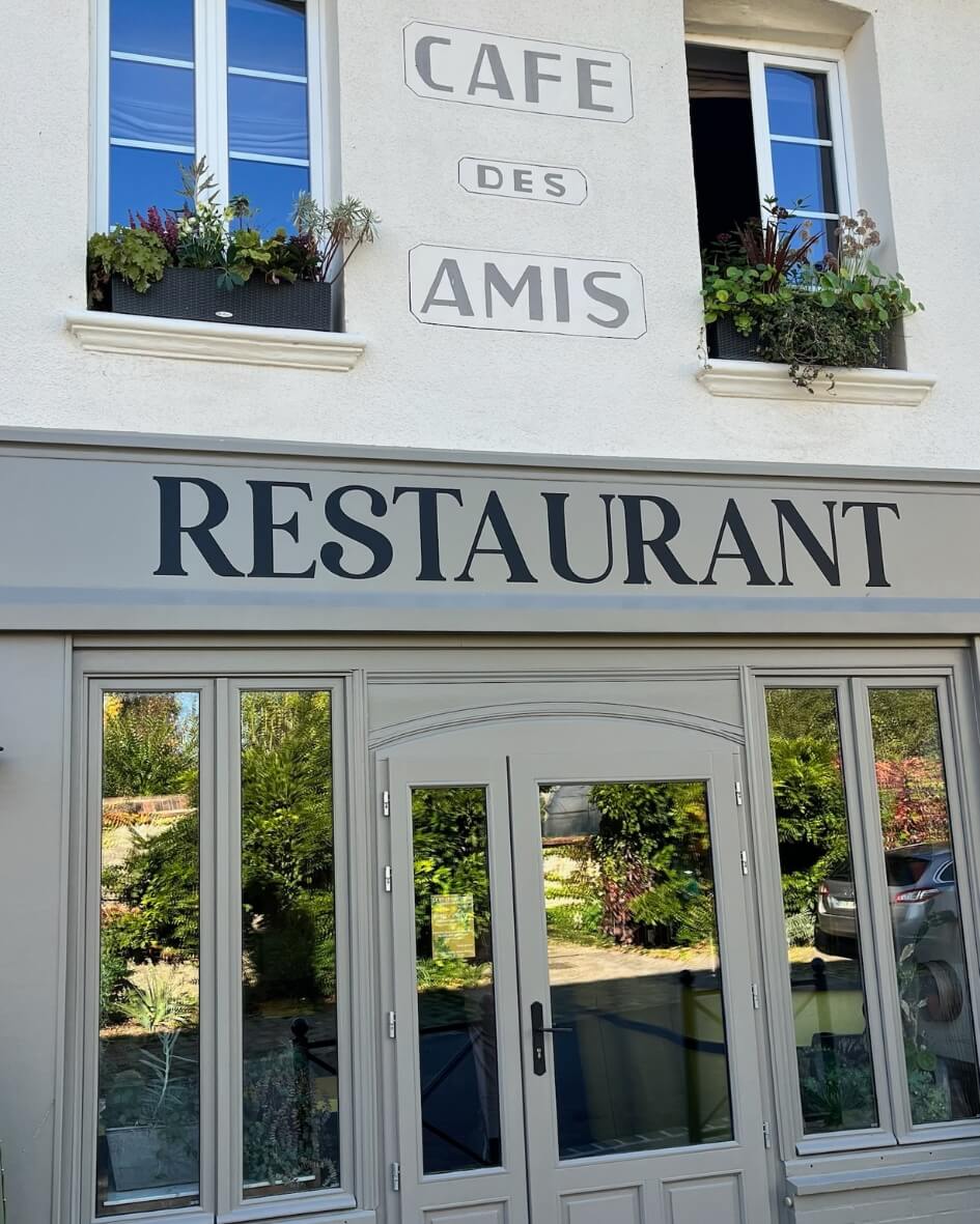 Cafe des Amis Restaurant in Normandy, France with bright French windows and potted flowers.