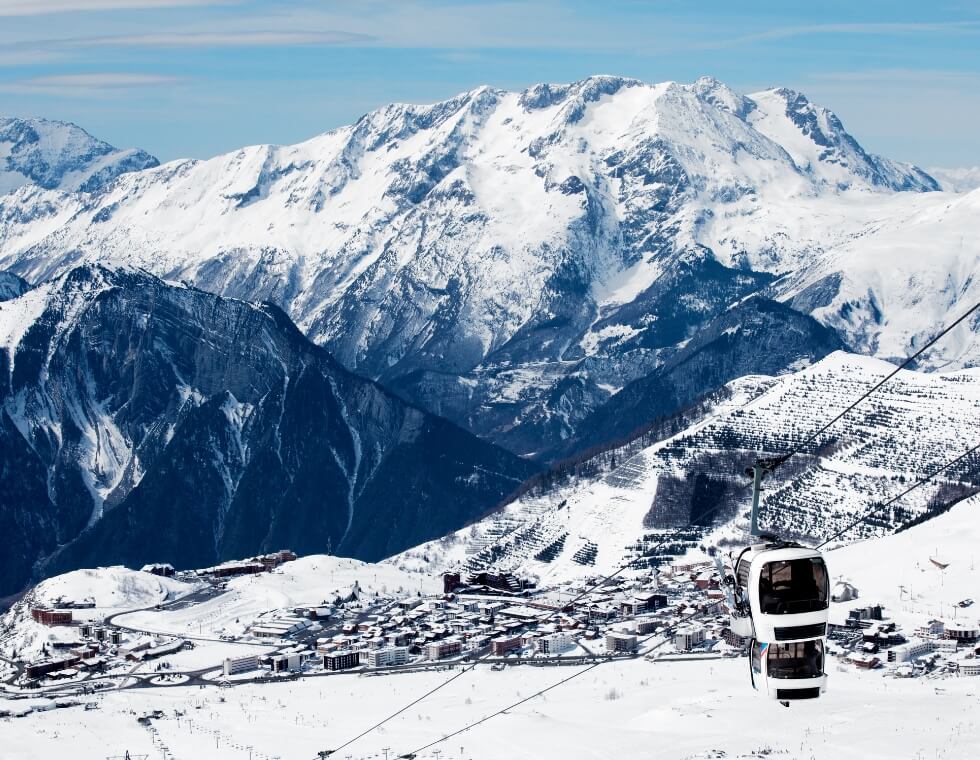 Alpe d’Huez ski resort in the French Alps with snowy peaks and a covered ski lift.