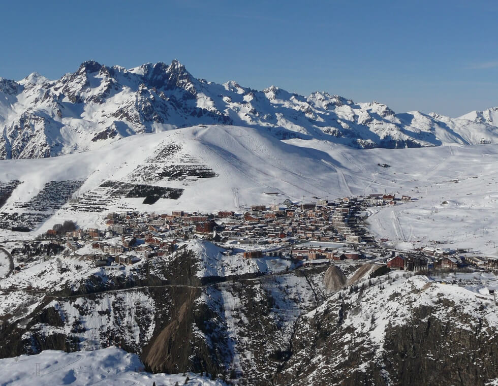 Alpe d’Huez ski resort in the distance, surrounded by snowy mountains in the French Alps.
