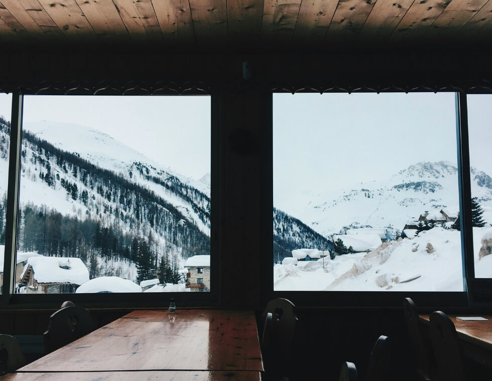 Long wooden dining tables beside a large window overlooking snowy mountains at Val d’Isère in the French Alps.