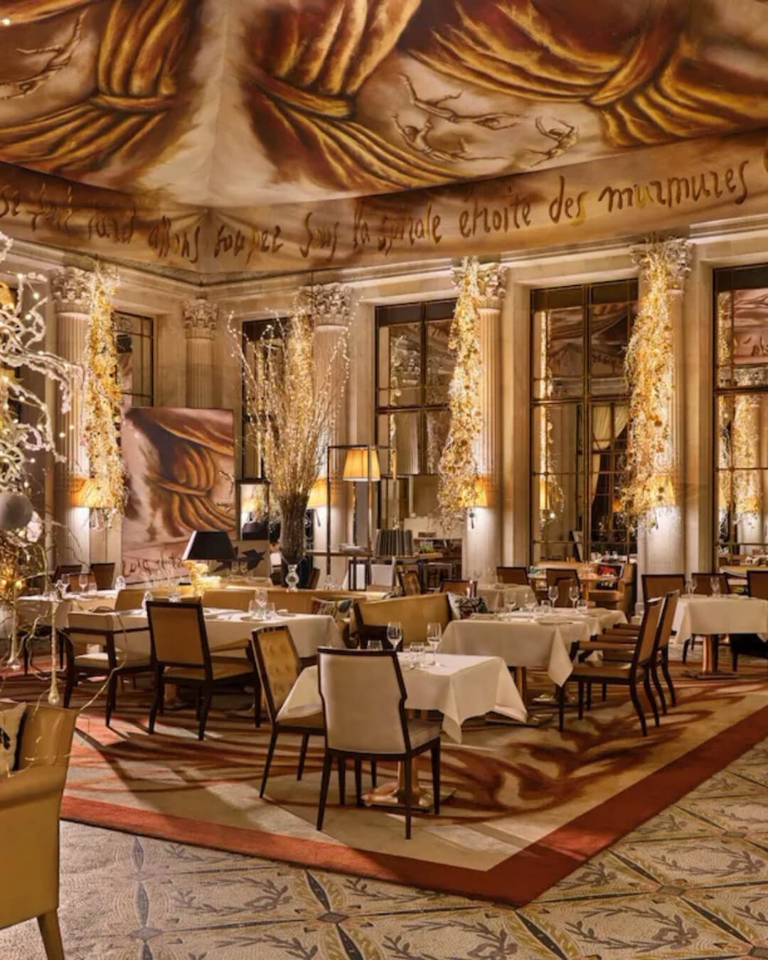 Dining room at Le Meurice hotel in Paris decorated for the holidays with warm, soft lighting.