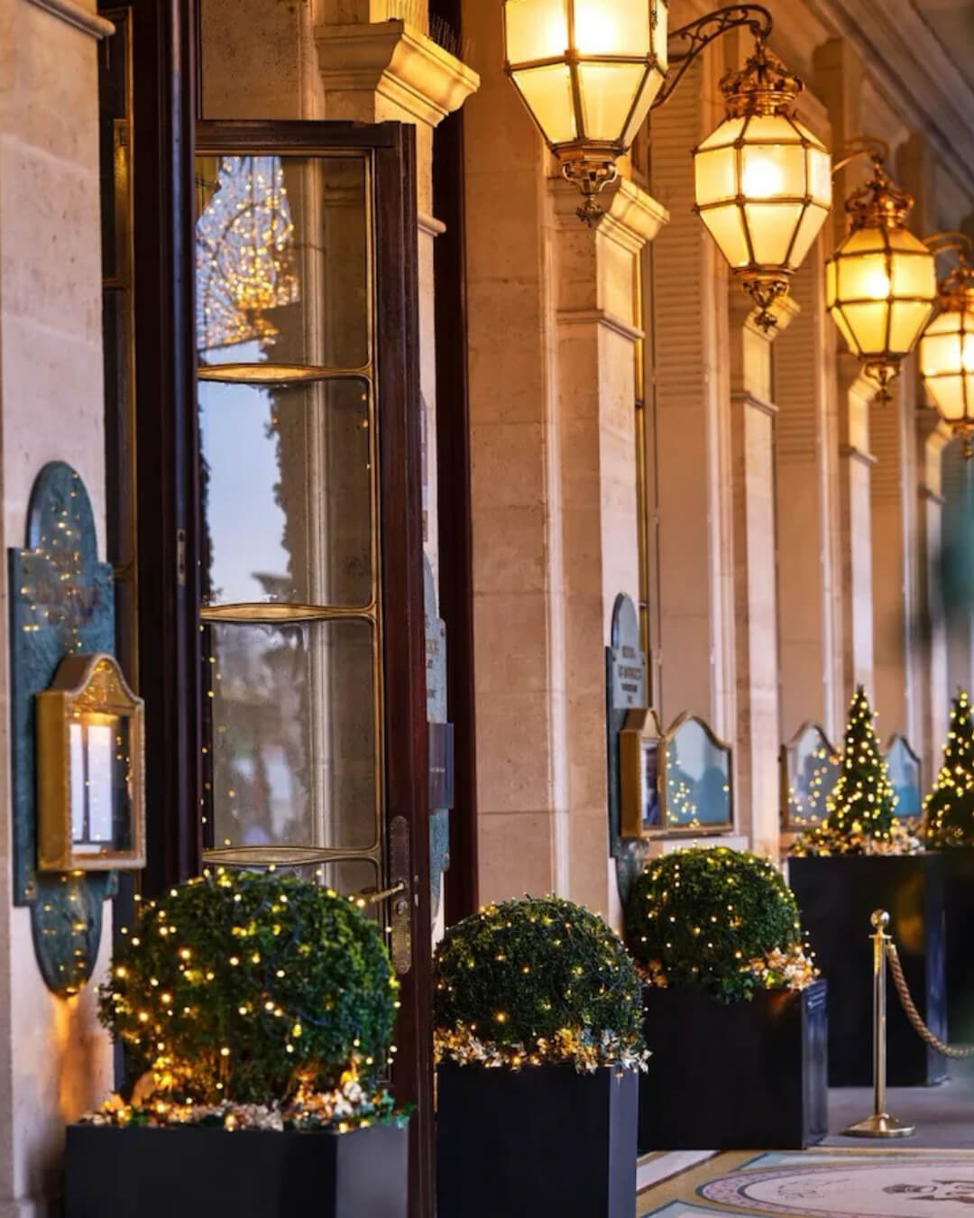Le Maurice hotel exterior featuring art deco lanterns and potted greenery with holiday lights in Paris, France.