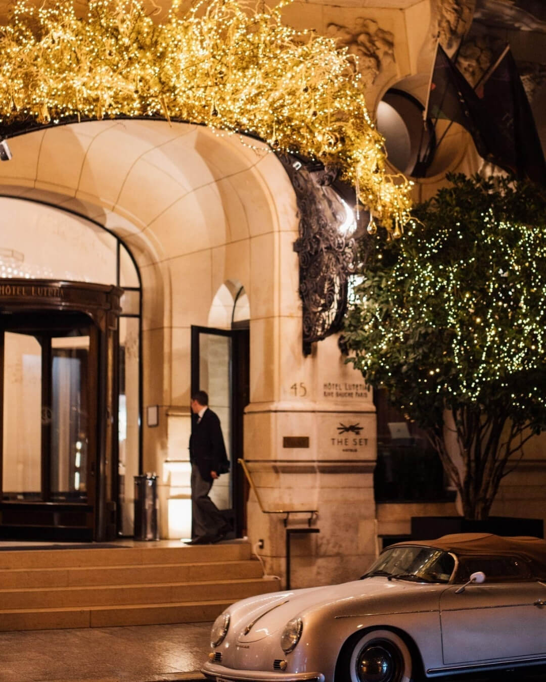 Exterior of the Lutetia Hotel in Paris with glowing holiday lights above a vintage car.
