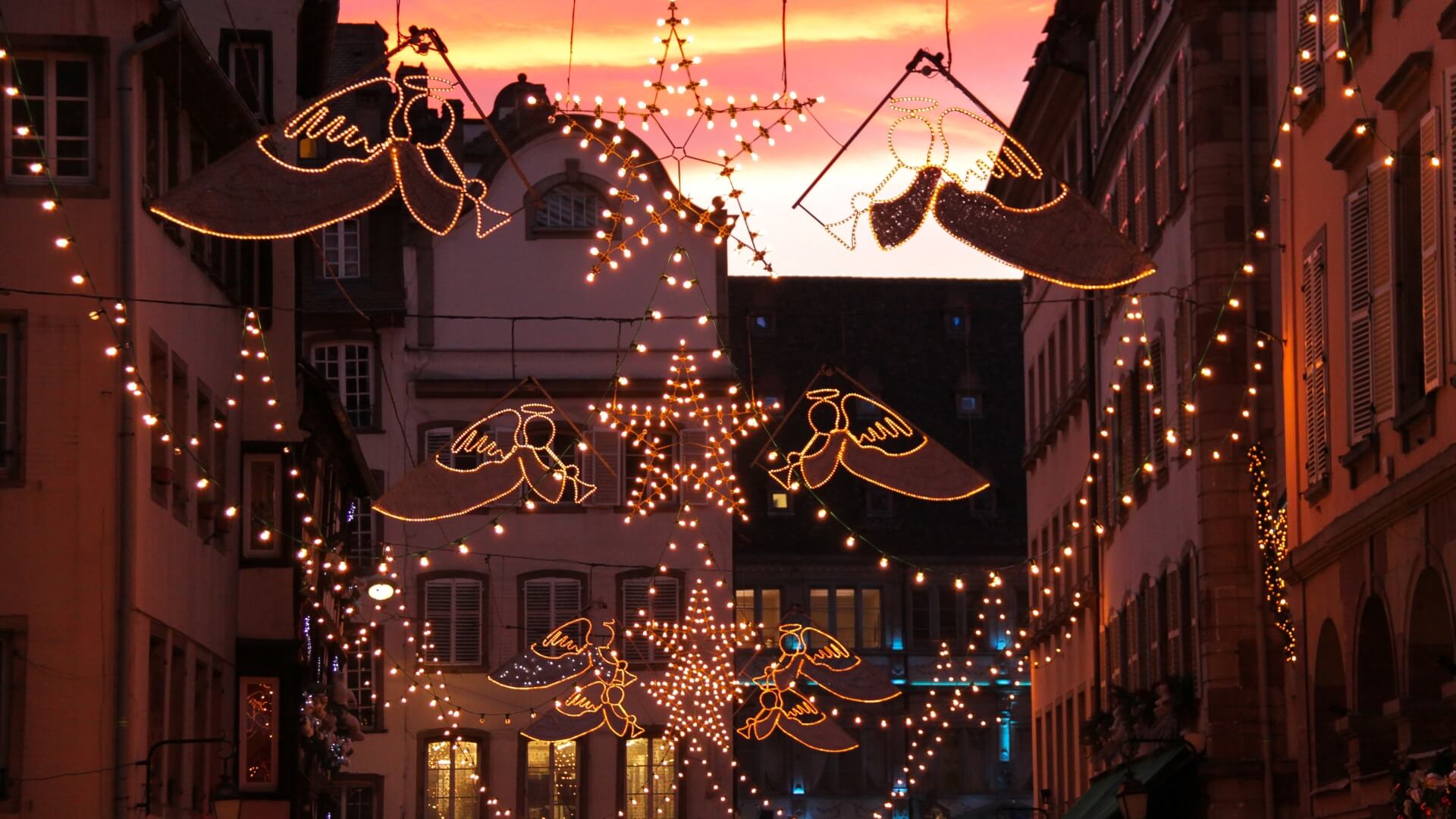 Hanging holiday lights and Christmas angel decorations in Strasbourg, France at sunset.