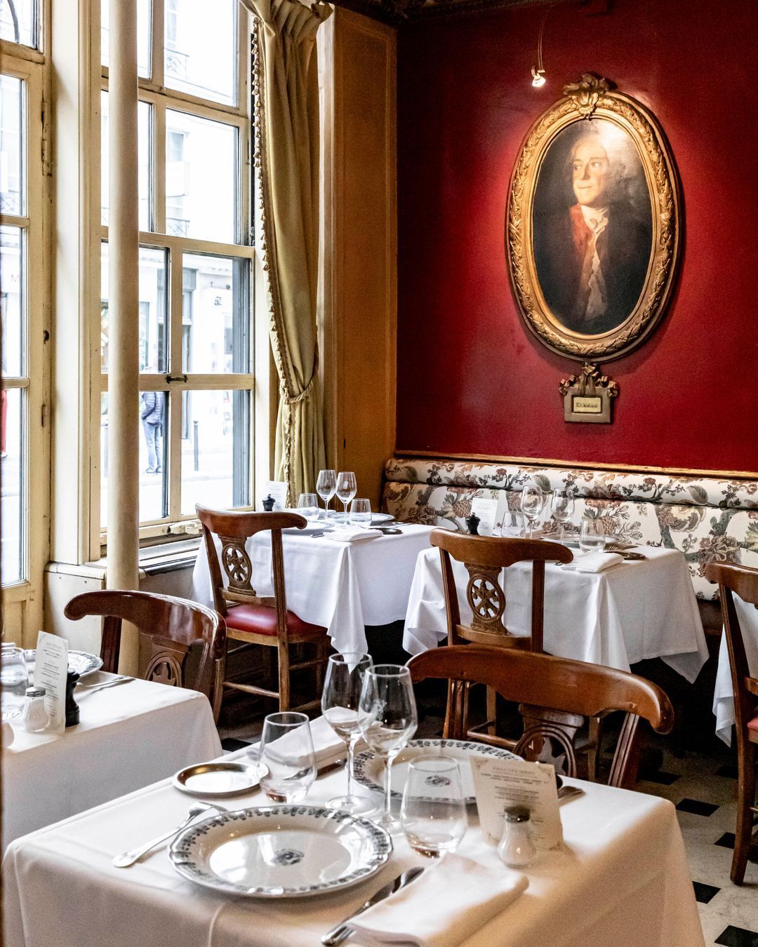 Le Procope restaurant in Paris, France with charming dining tables, framed art, and bright natural light.