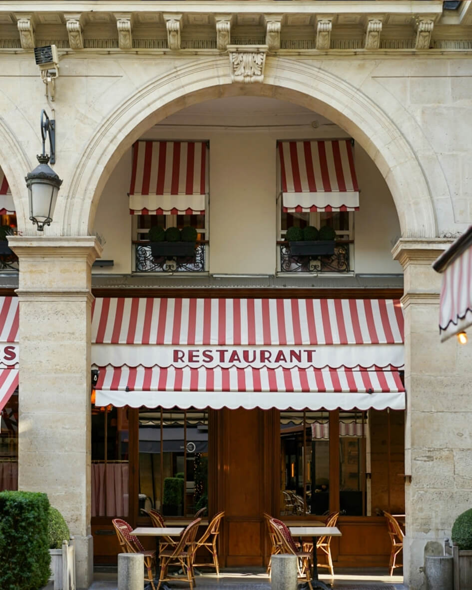 French bistro in Paris, France with terrace dining beneath a red and white awning.