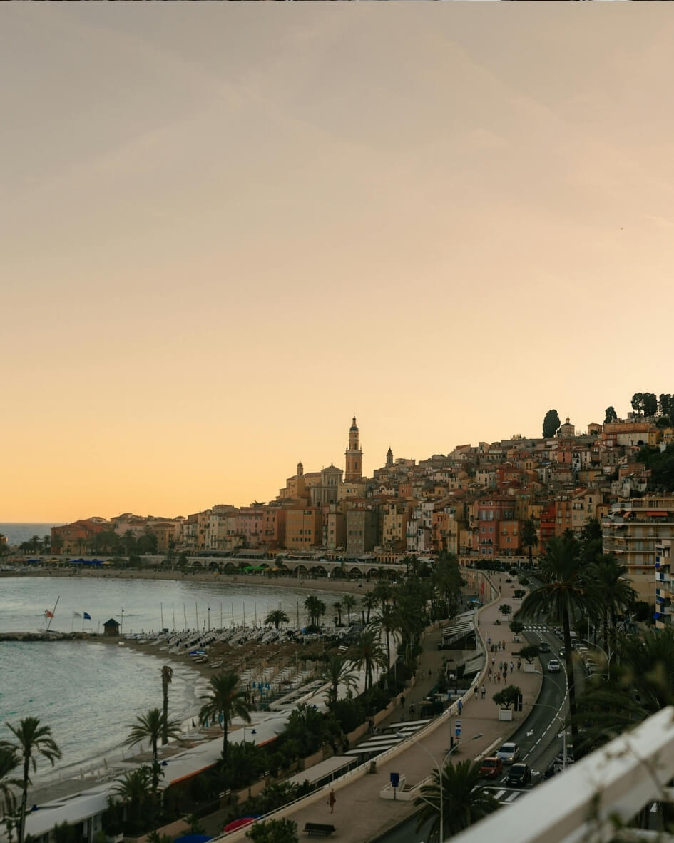 Sunset over the French Riviera along the Mediterranean Sea, with palm trees and empty sidewalks.