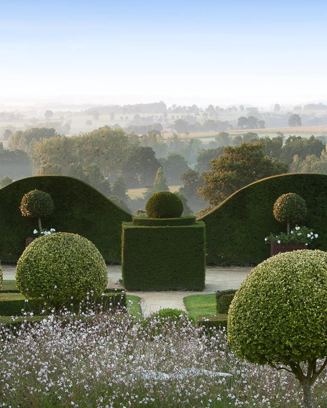 Topiary garden in La Ballue, Brittany with symmetrical manicured hedges and distant rolling hills.