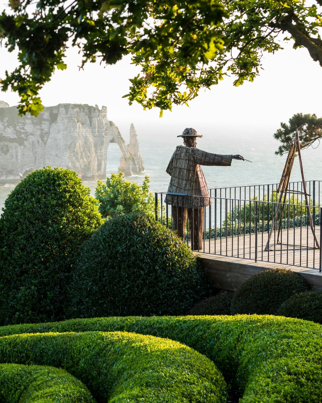 Statue of Claude Monet overlooking the cliffs of Etretat, beside a lush Topiary garden in Normandy, France.