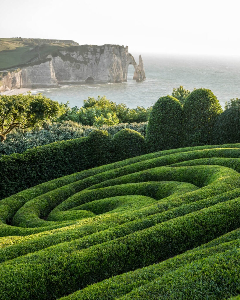 Manicured topiary hedges in a spiral design in Étretat, Normandy, overlooking coastline cliffs.