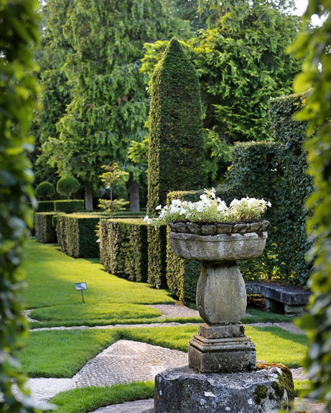 The Gardens of Eyrignac Manor with topiary style hedges, lush grass, and a historic stone flower pot.