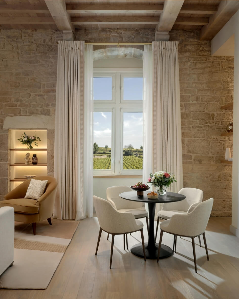 The Château la Commaraine Hotel in Burgundy, France, featuring historic architecture and a window view overlooking a vineyard.