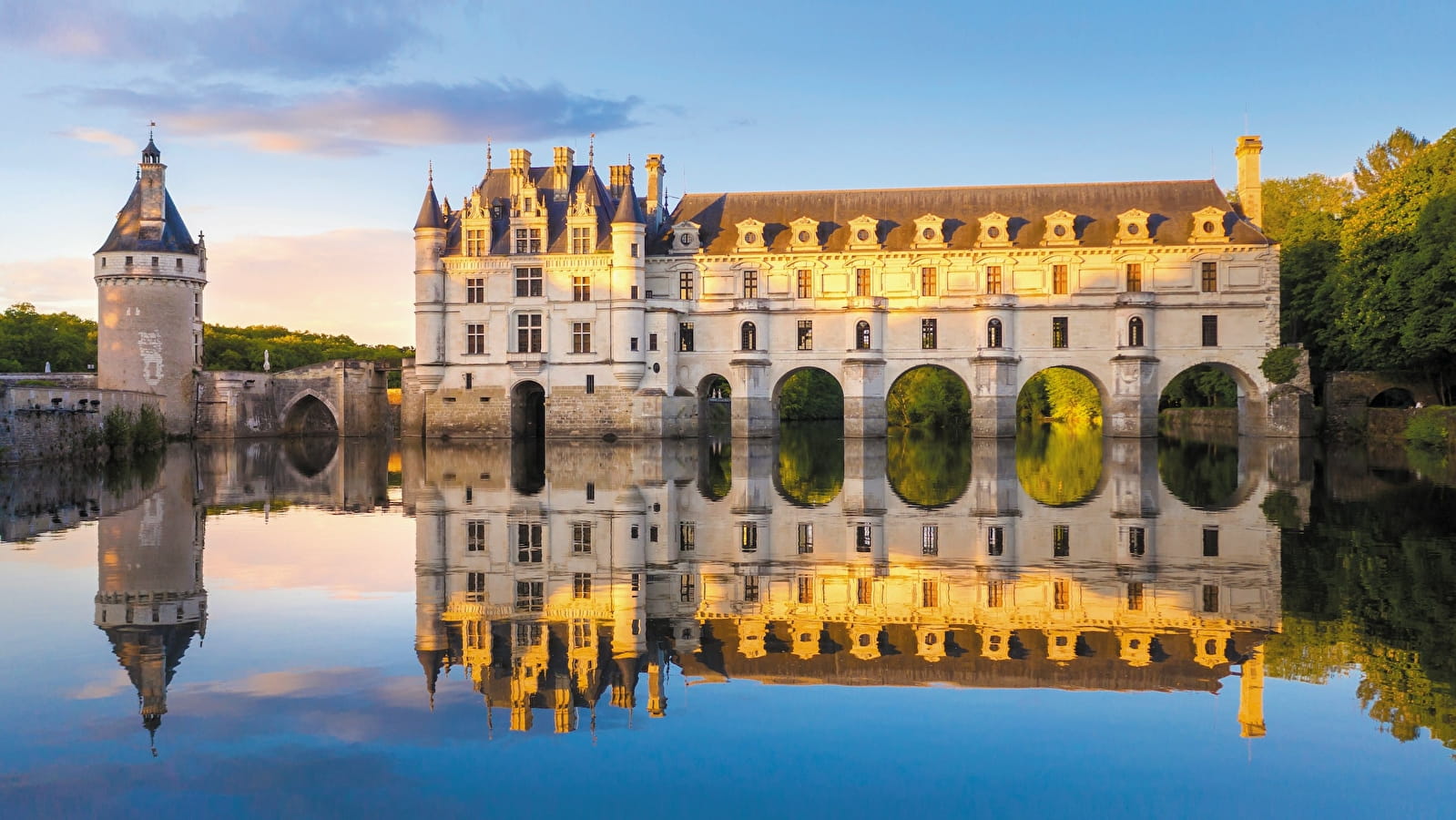 Historic Chateau in the Loire Valley, France above a calm lake at sunset.