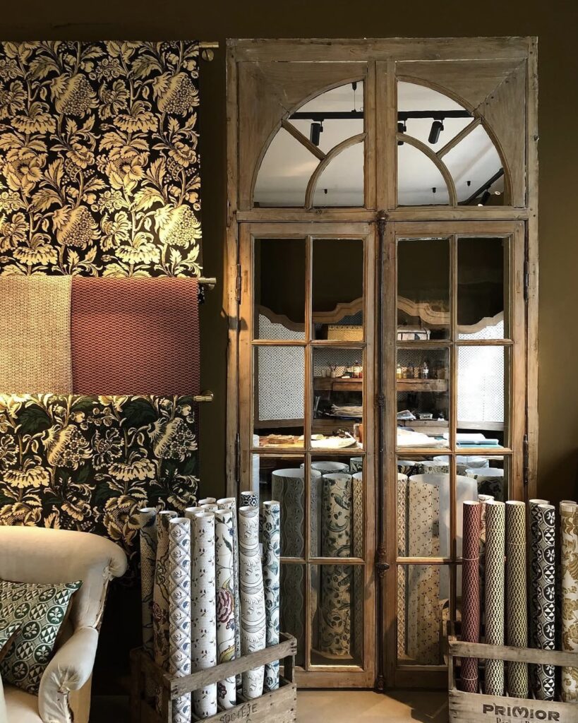 Ornate decorative rolls of paper on display at a Parisian atelier beside mirrored French doors.