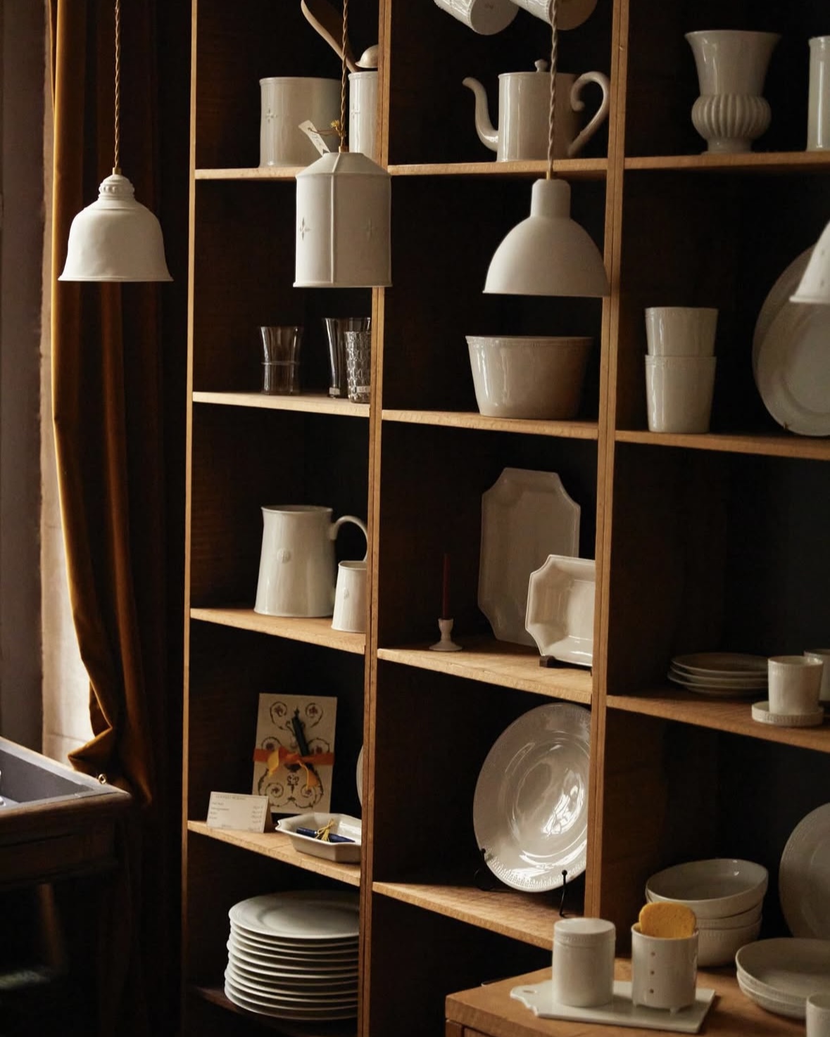 White ceramic dishes displayed on wooden shelves, beneath hanging lamps.