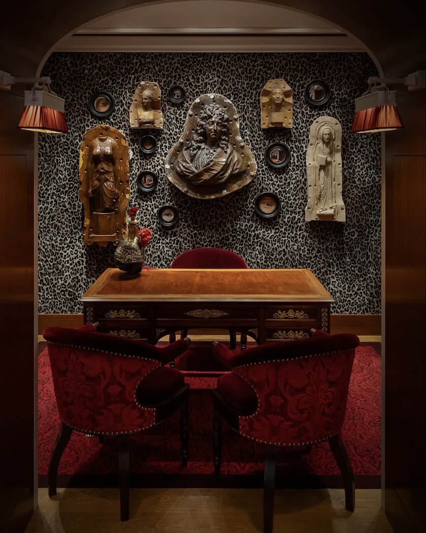 Desk and chairs in a statue-lined room at the Jacques Marie Mage boutique in Paris, with leopard-print walls.