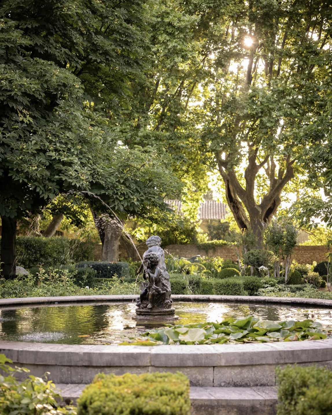 Mas de Chabran villa garden pond and cherub fountain surrounded by lush manicured greenery in Provence, France.