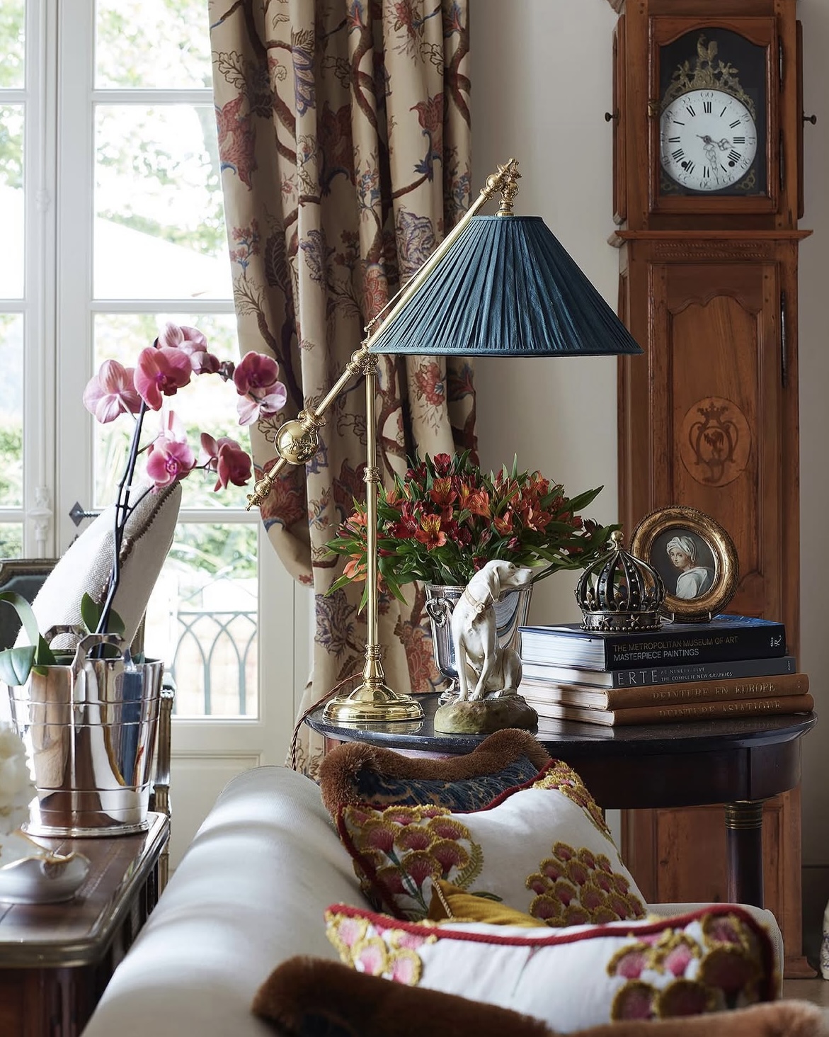 Villa salon interior in Poirriers, with cozy seating, potted orchids, and an antique grandfather clock.