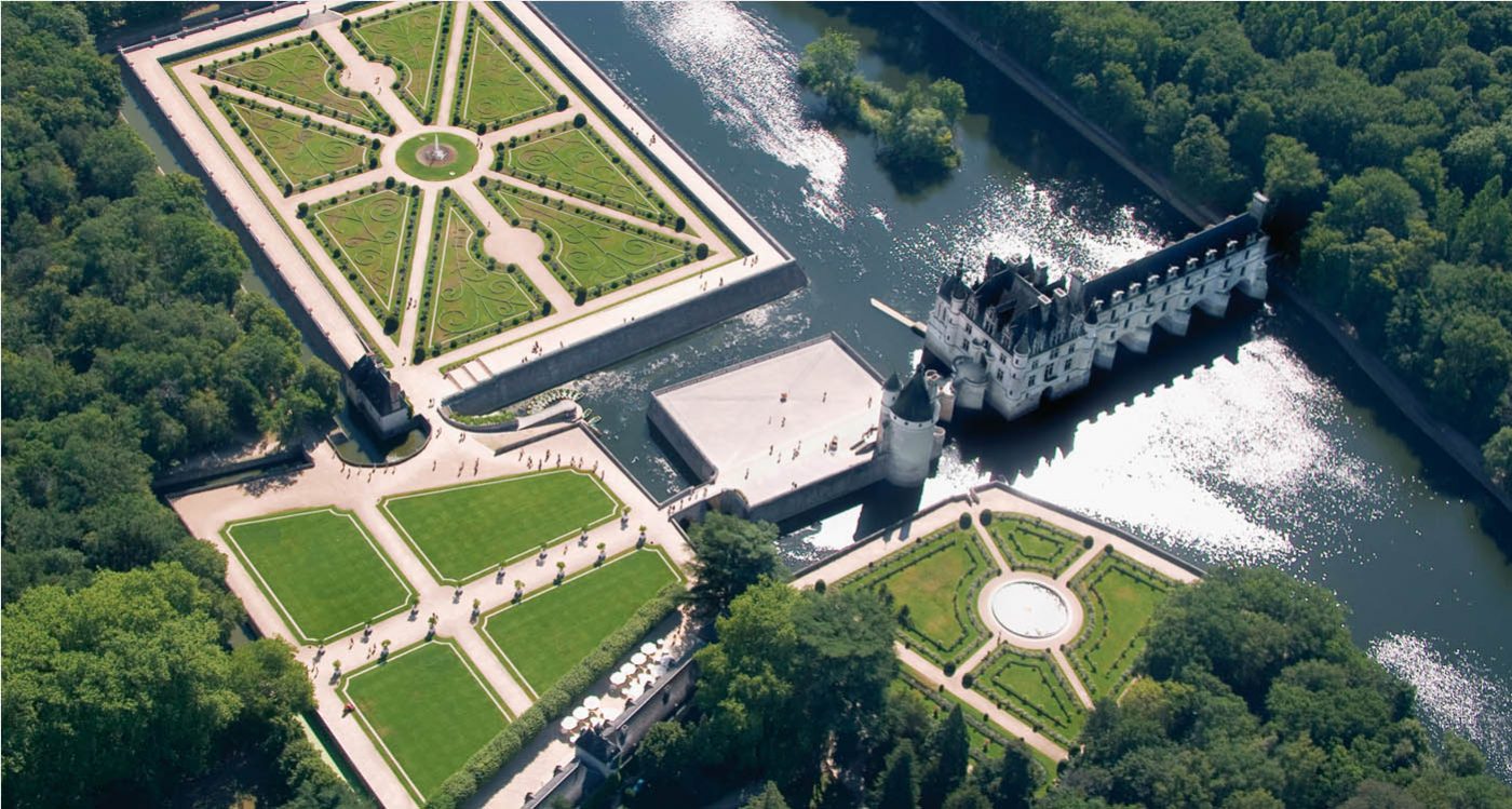 View of Chenonceau Château in the Loire Valley, France, with lush gardens and a flowing lake below.
