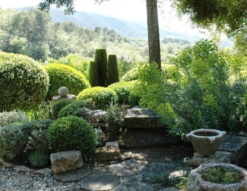 Manicured hedges and lush greenery next to a stone lookout with views of rolling hills in Provence, France.