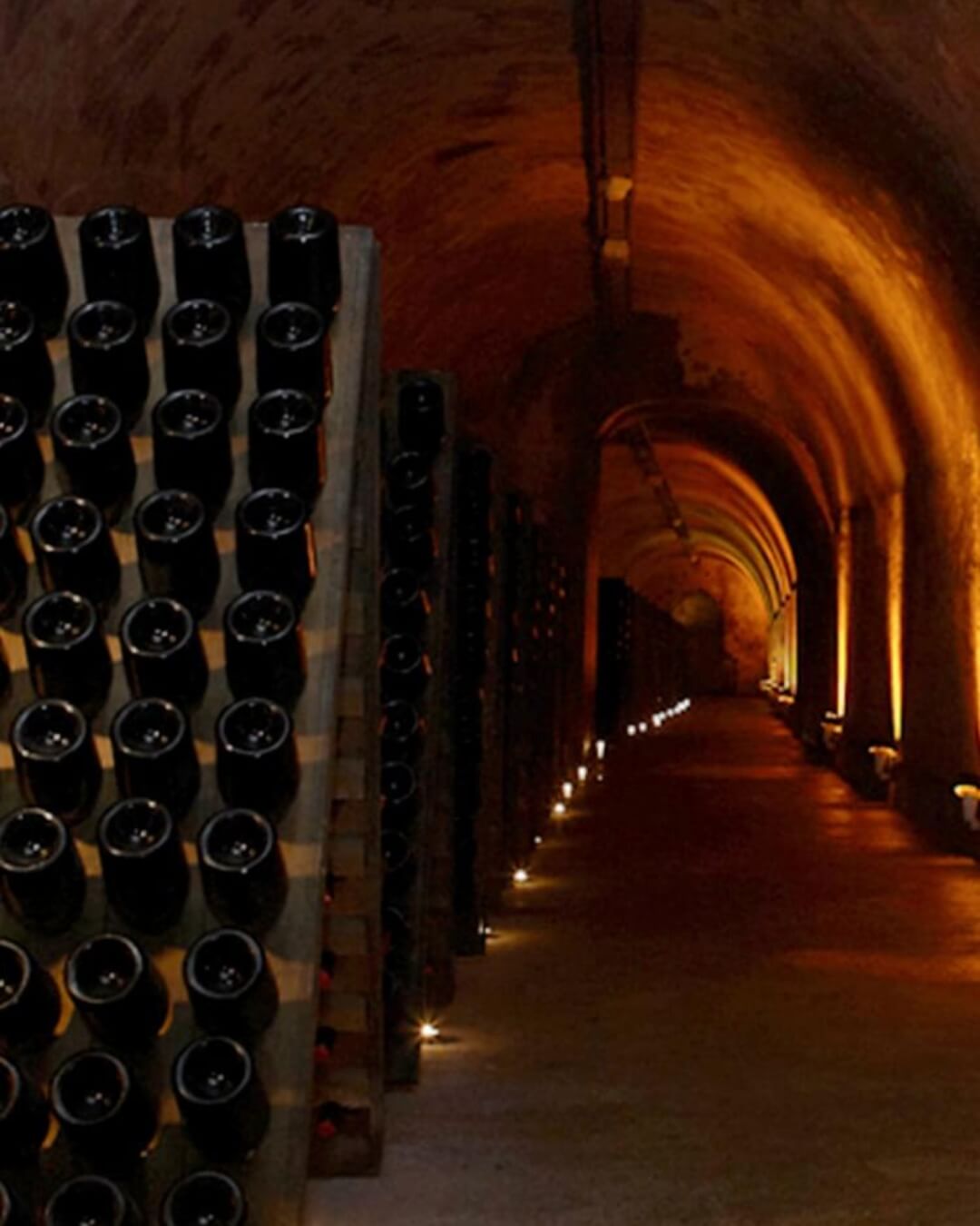 Dimly lit stone wine cellar in Champagne, France with rows of bottles stored upside down.
