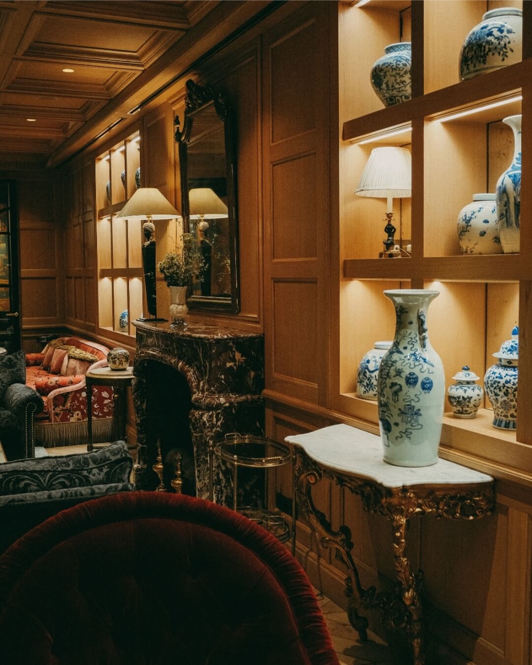 Relais Christine luxury hotel salon in Paris with shelves of antique ceramic vases, a marble fireplace, and antique furniture.