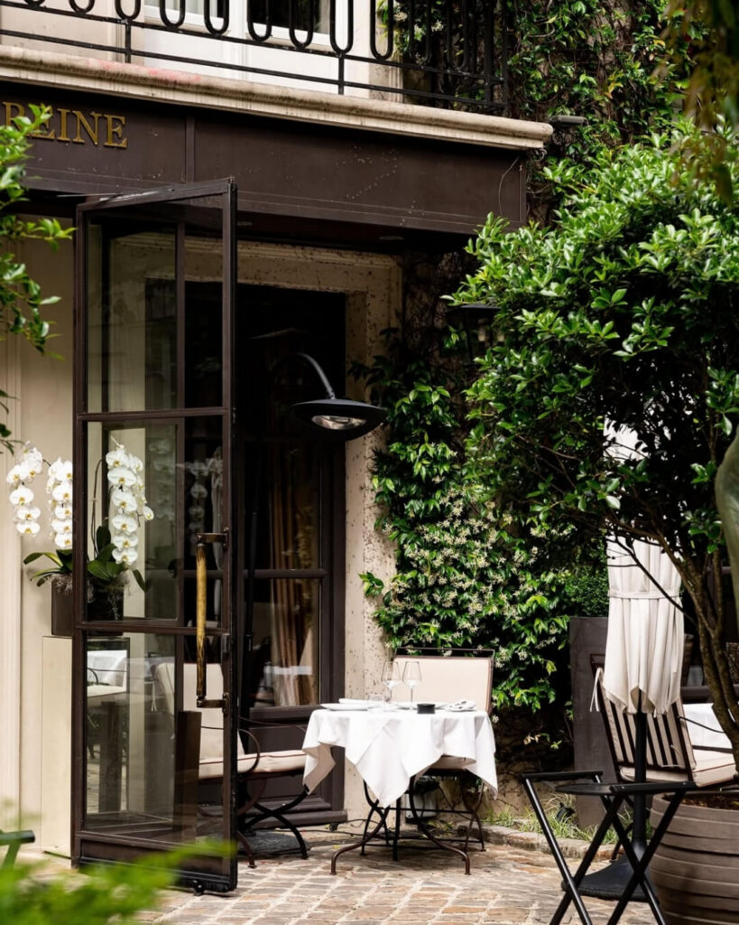 Courtyard of Michelin-starred restaurant Anne in the Marais, Paris, featuring jasmine plants and small trees along the outdoor seating area.