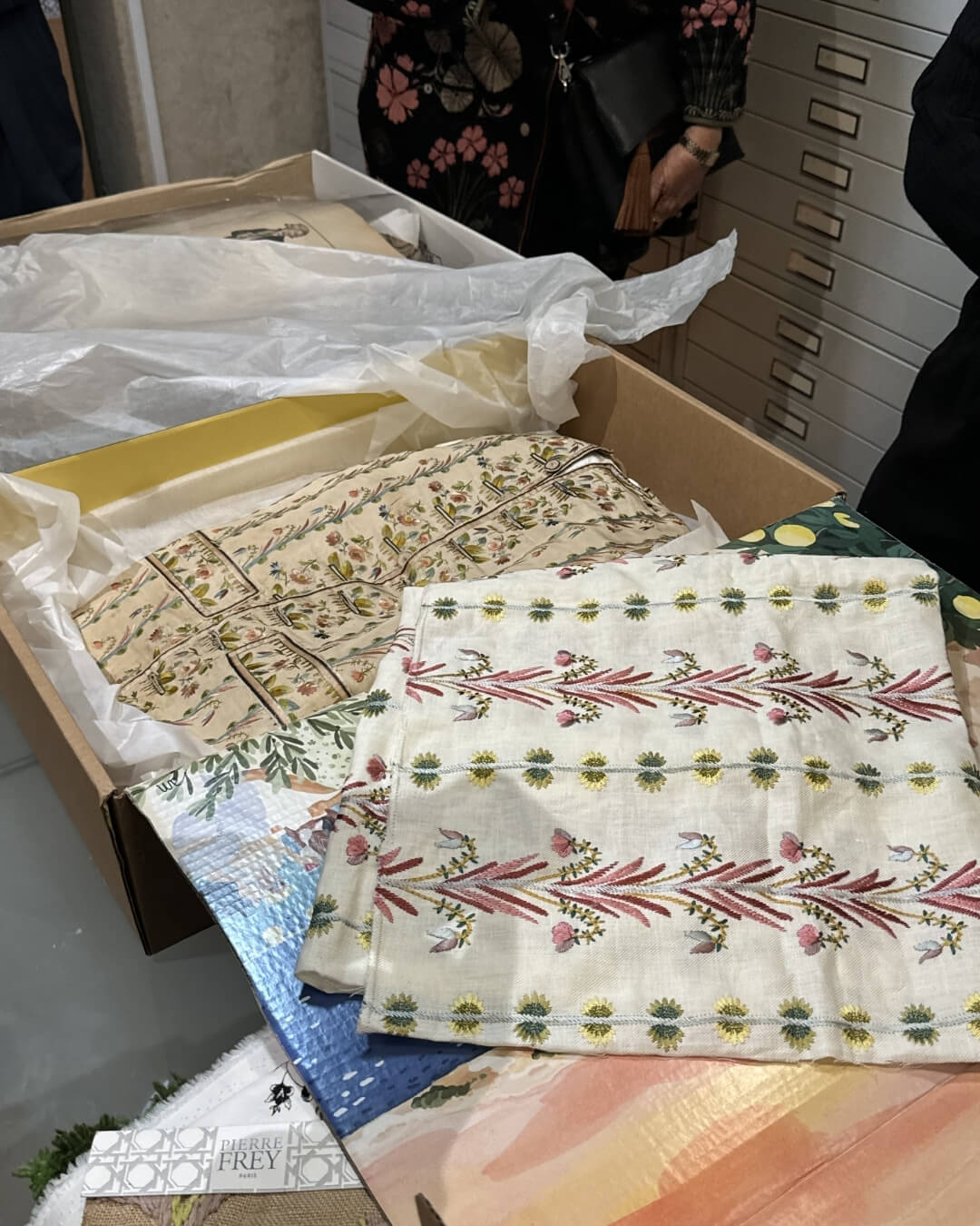 Antique hand-sewn textiles on display in boxes at a Parisian antique market.