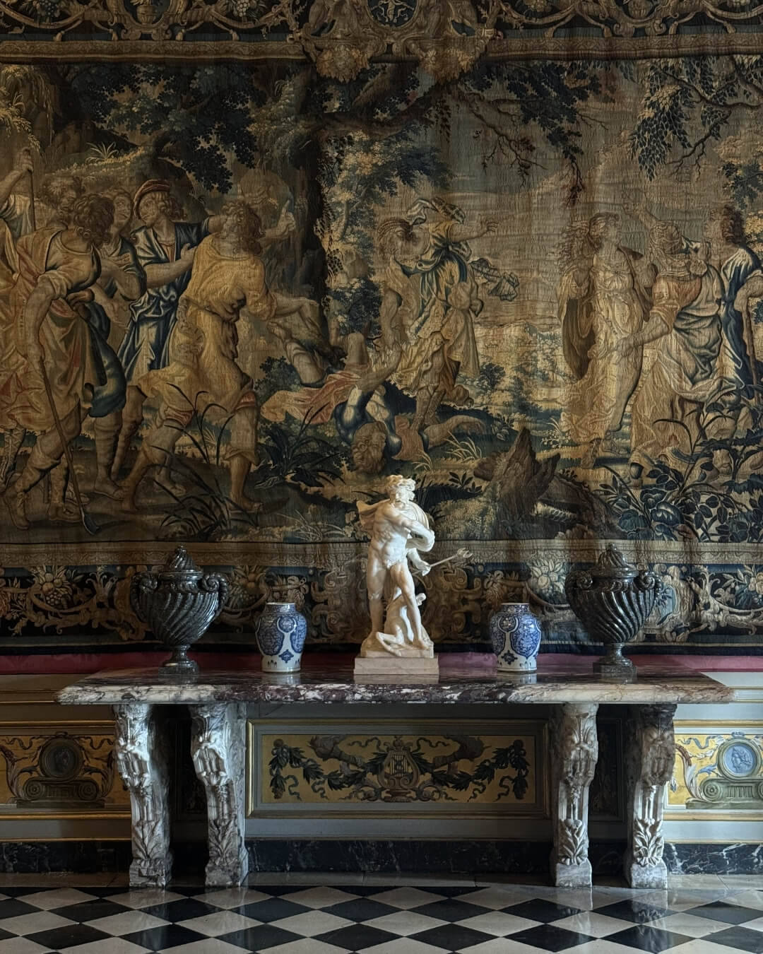 Antique woven tapestry hanging above a marble table with French antique statues and vases.