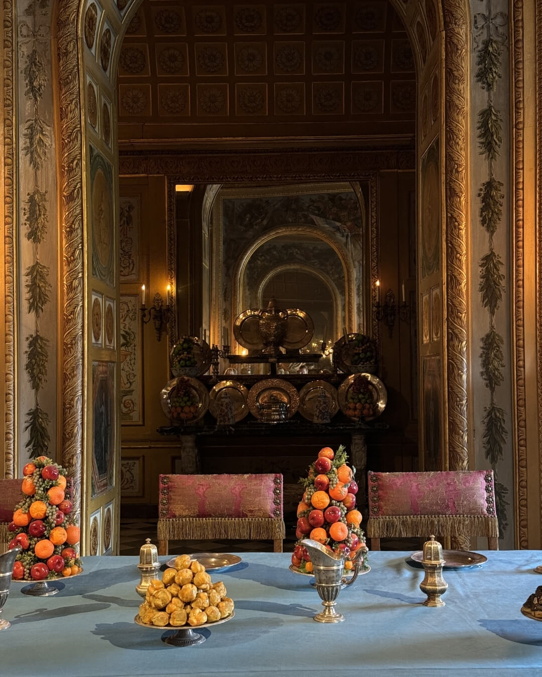 French chateau dining room interior with gilded walls, silk upholstered chairs, and plates of fruit.