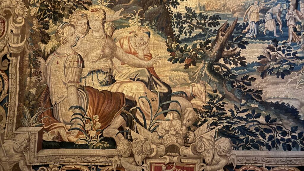 French antique woven tapestry with blue and red accents, depicting people lying on grass with animals.