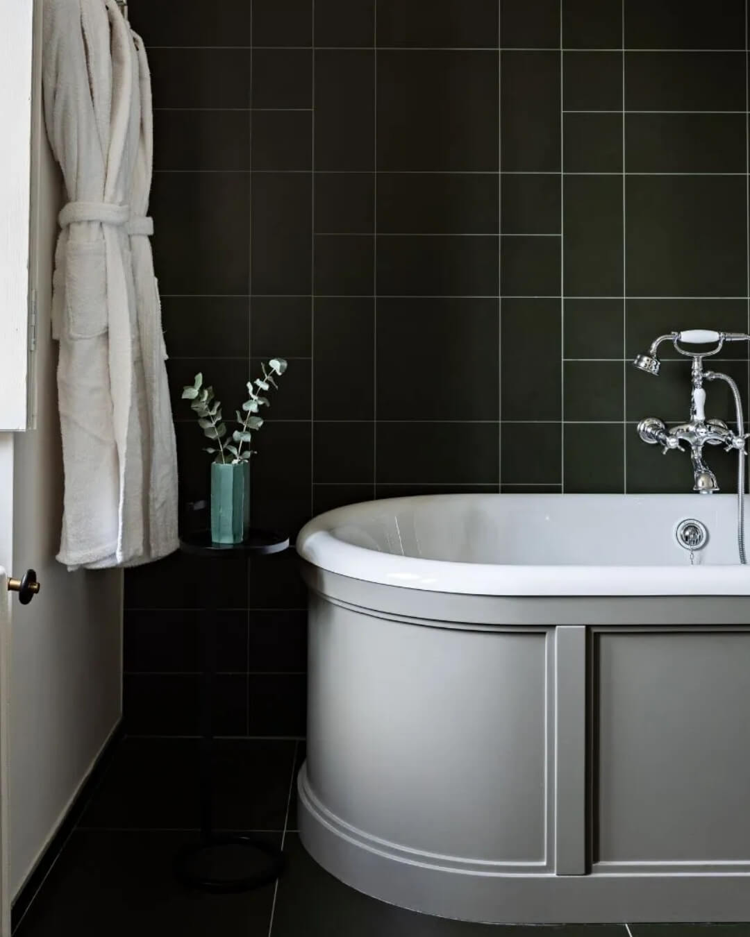 Bathroom interior at Domaine de Primard hotel with an iron tub, forest green tiles, and fresh eucalyptus.