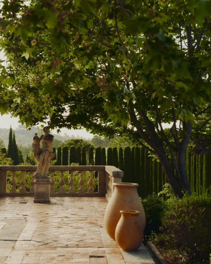 Hotel garden terrace in La Cavalerie, France with terracotta planters, stone statues, and views of lush manicured hedges.
