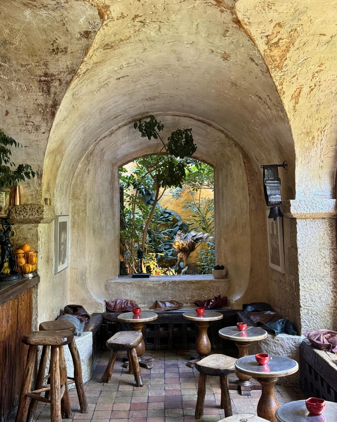 La Colombe d'Or café interior with intimate tables and benches beside an open window facing a lush garden.