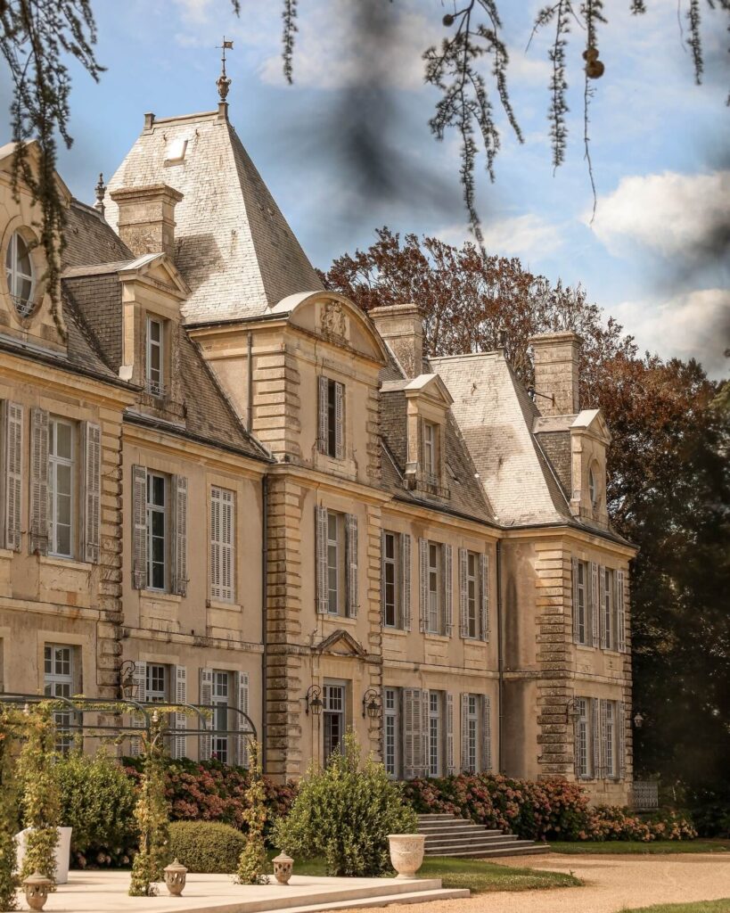 Chateau de Curzay exterior with rows of French windows, textured stone detailing, and a lush garden before the entrance.
