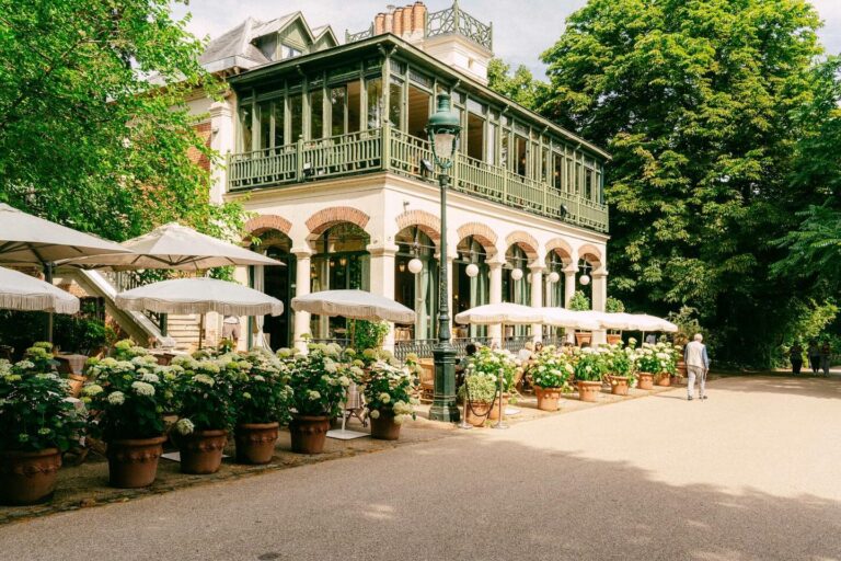 ORA Farm House restaurant exterior in Parc Buttes-Chaumont, Paris with a green painted sunroom, potted hydrangeas, and white umbrellas.