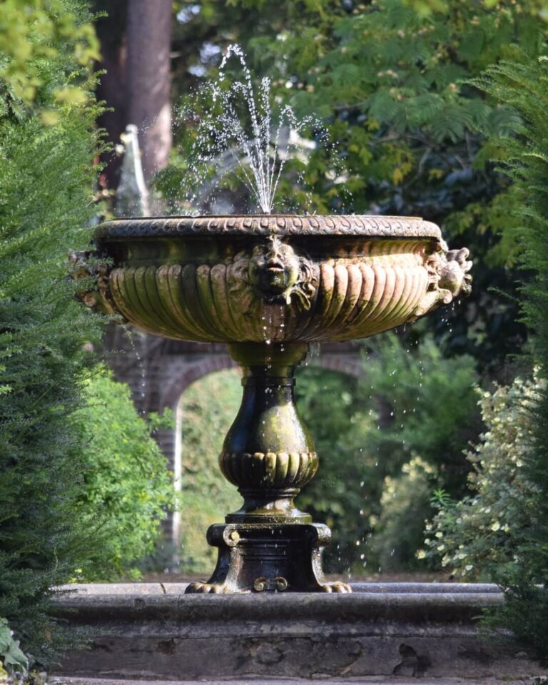 Ornate garden fountain and pond surrounded by lush greenery and trees in Sussex, England.