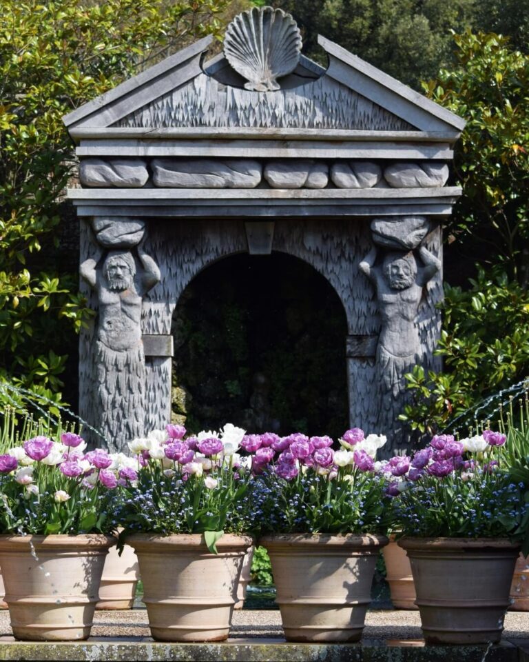 Ornate stone garden gazebo and potted purple tulips in Sussex, England.