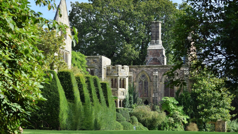 English garden in Sussex with lush manicured hedges and historic stone church.
