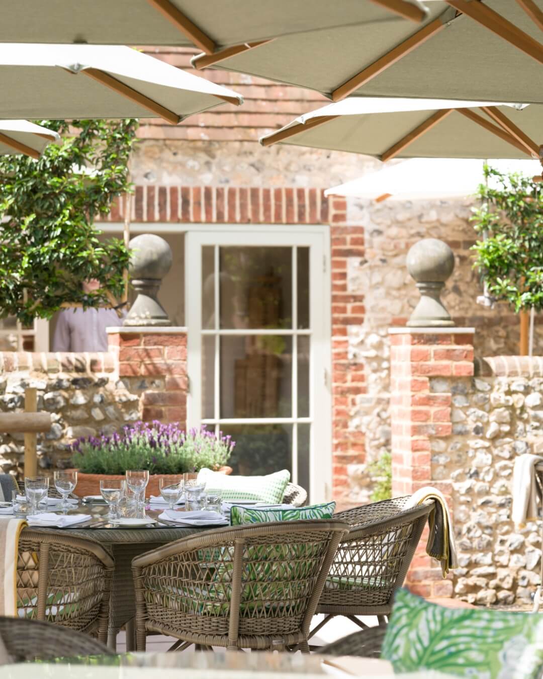 Terrace dining in the Star Hotel garden in Sussex, England with wicker chairs and flax colored parasols.