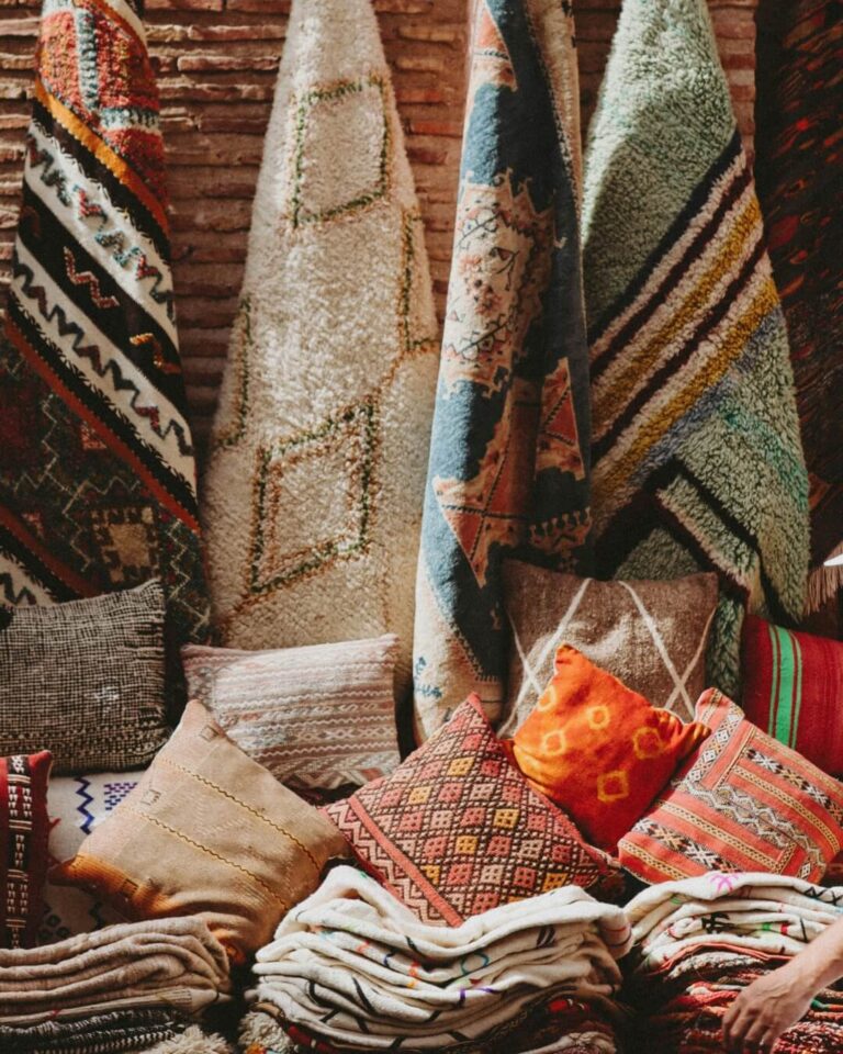 Folded linens, pillows, and hanging hugs on display at a market in Morocco.